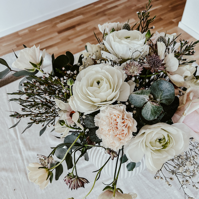 Bild på en blombukett i ljusa toner. I buketten finns blandannat nejlikor, ranunklar, fjärilsranunklar, vaxblommor, stjärnflocka och eukalyptus.